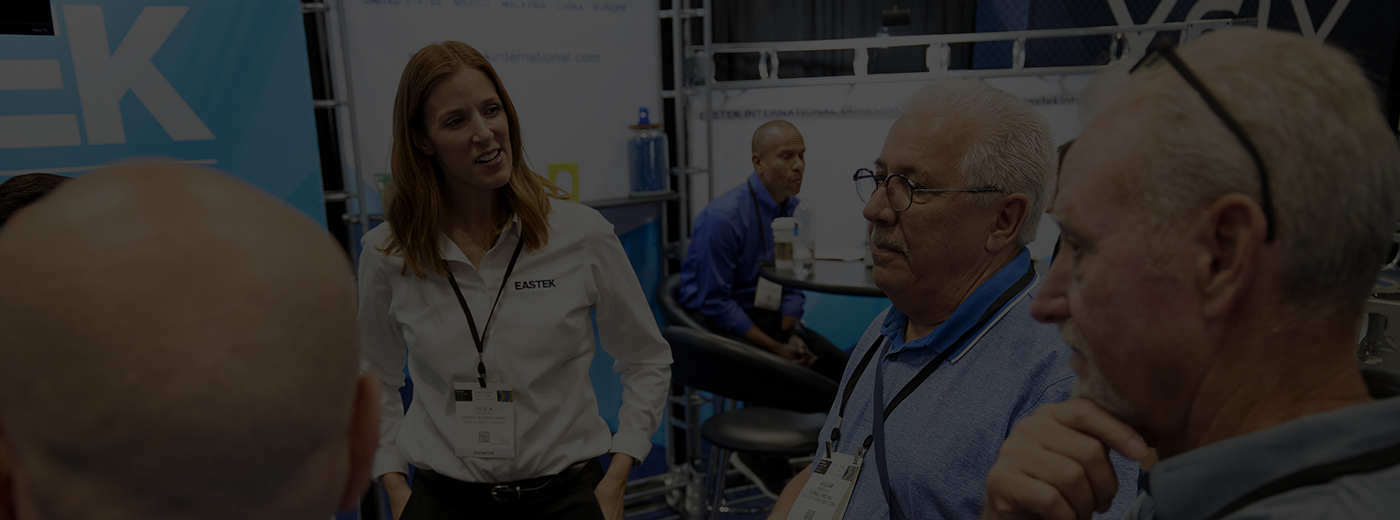 A diverse group of individuals engaged in conversation at a bustling trade show, surrounded by various displays and booths.